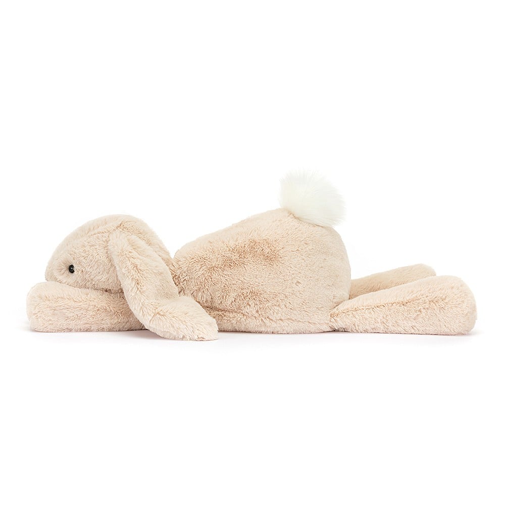 A side view of Jellycat Smudge Rabbit with oatmeal coloured fur, long floppy ears and a white fluffy tail, lying stretched out.