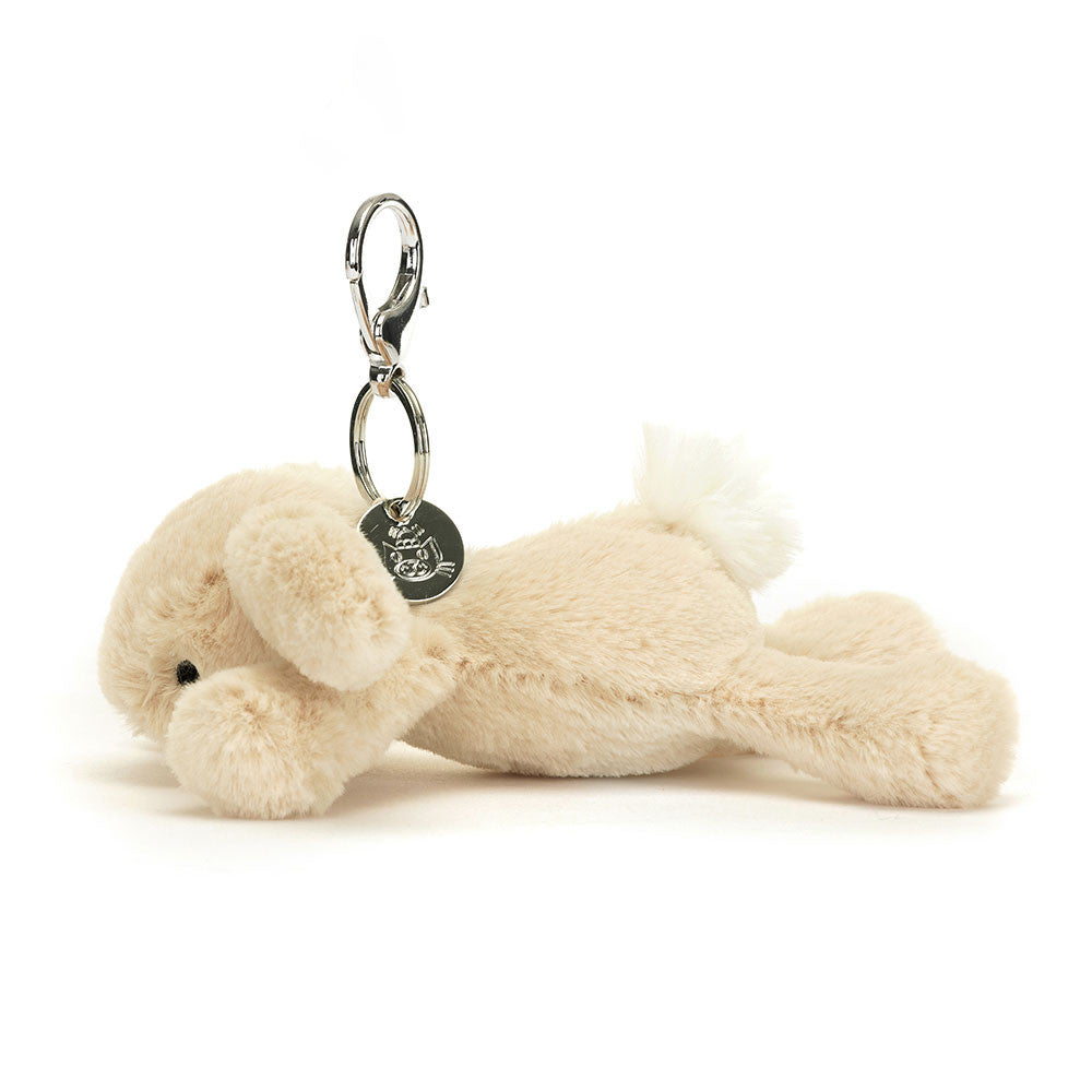 Side view of Jellycat Smudge Rabbit Bag Charm (16cm x 13cm), featuring its soft beige fur, long floppy ears, and fluffy pompom tail attached to a silver claw clip.