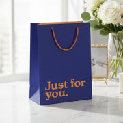Navy blue slogan gift bag in lifestyle setting with white roses and vase.