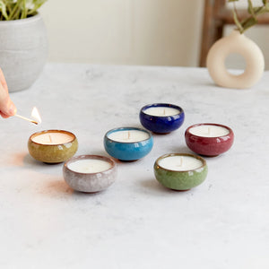 Hand lighting a Kiln ceramic tea light from a set of six glazed candles in green, blue, red, purple, grey, and ochre hues.
