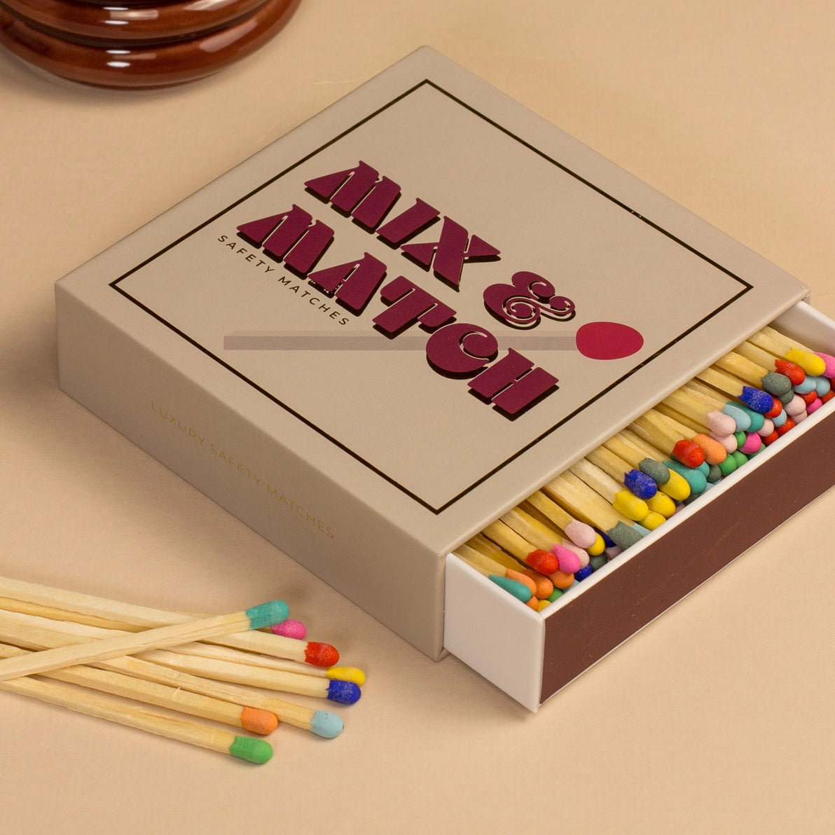 Angled front view of the Kiln Mix & Match luxury matchbox, partially open to reveal colourful tipped safety matches spilling onto a neutral surface.