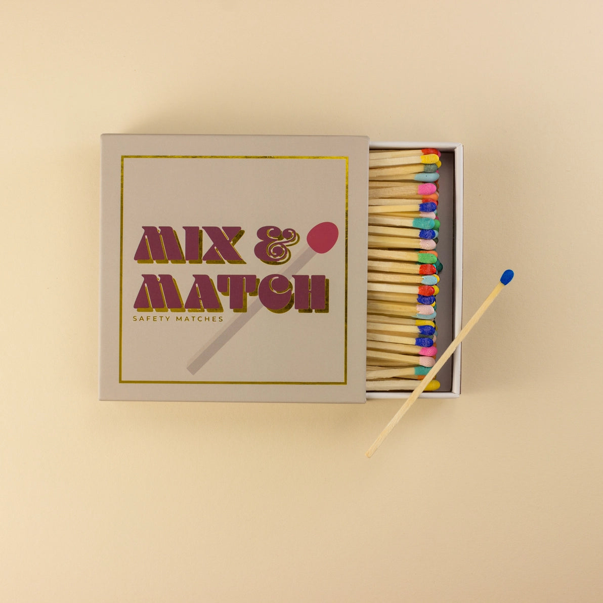 Top-down view of the Kiln Mix & Match safety matchbox with lid open, showing neatly arranged multicoloured match heads and bold gold-foiled typography.