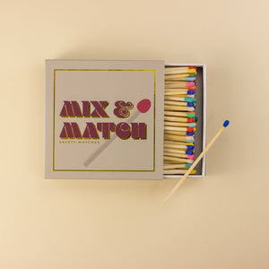 Top-down view of the Kiln Mix & Match safety matchbox with lid open, showing neatly arranged multicoloured match heads and bold gold-foiled typography.