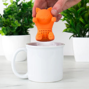 Hand placing orange cat-shaped Kit-Tea Infuser into white mug.
