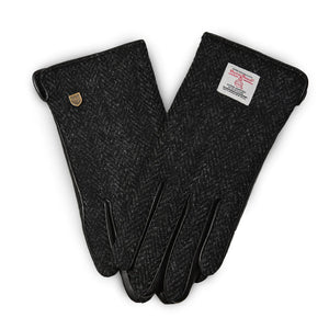 Pair of ladies gloves made from black herringbone Harris Tweed® with genuine leather trim, shown from the front with branded labels on the cuff.