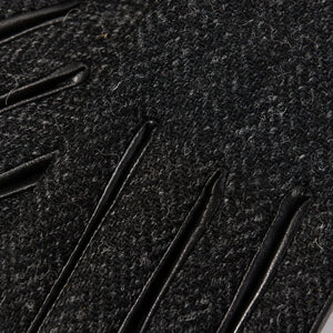 Macro shot of black herringbone Harris Tweed® fabric with raised leather finger detailing on ladies glove.