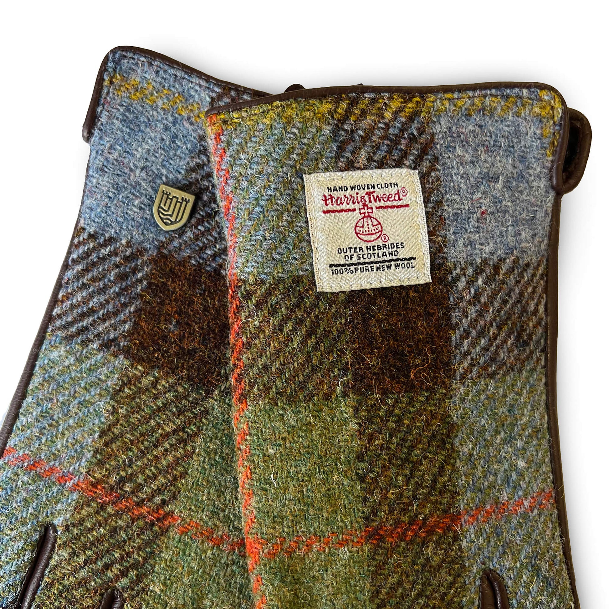 Detailed view of Harris Tweed® certification label on chestnut and blue tartan gloves with crest emblem.