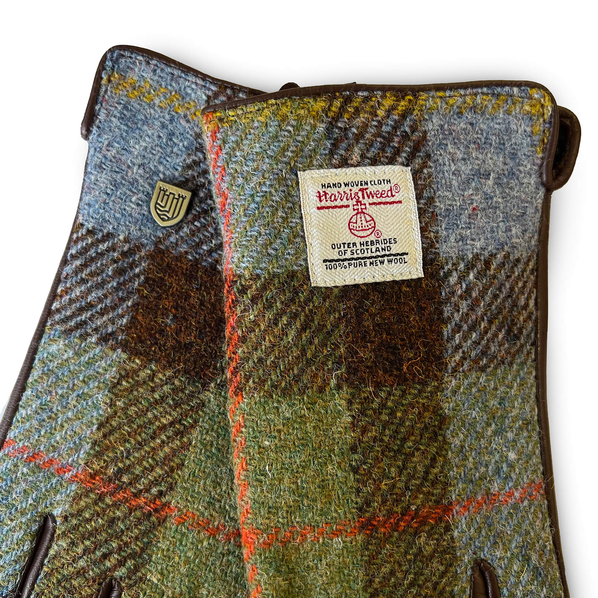 Detailed view of Harris Tweed® certification label on chestnut and blue tartan gloves with crest emblem.
