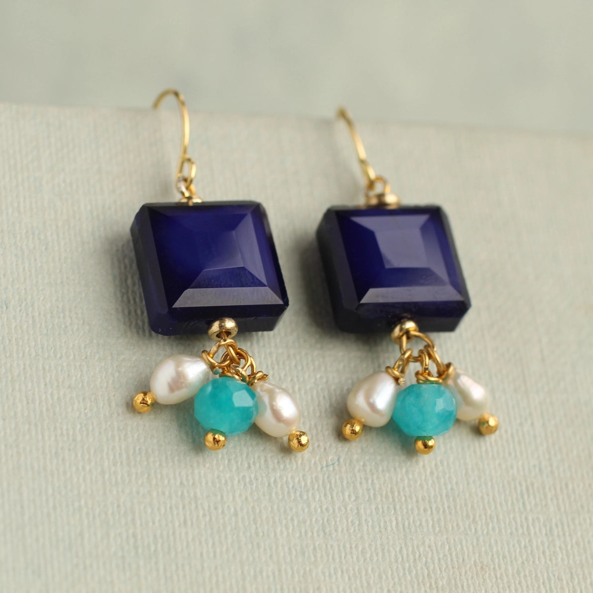 Front view of Lapis Lazuli blue charm earrings with square navy glass stones and dangling turquoise, aqua opal glass, and freshwater pearl charms on gold hooks.