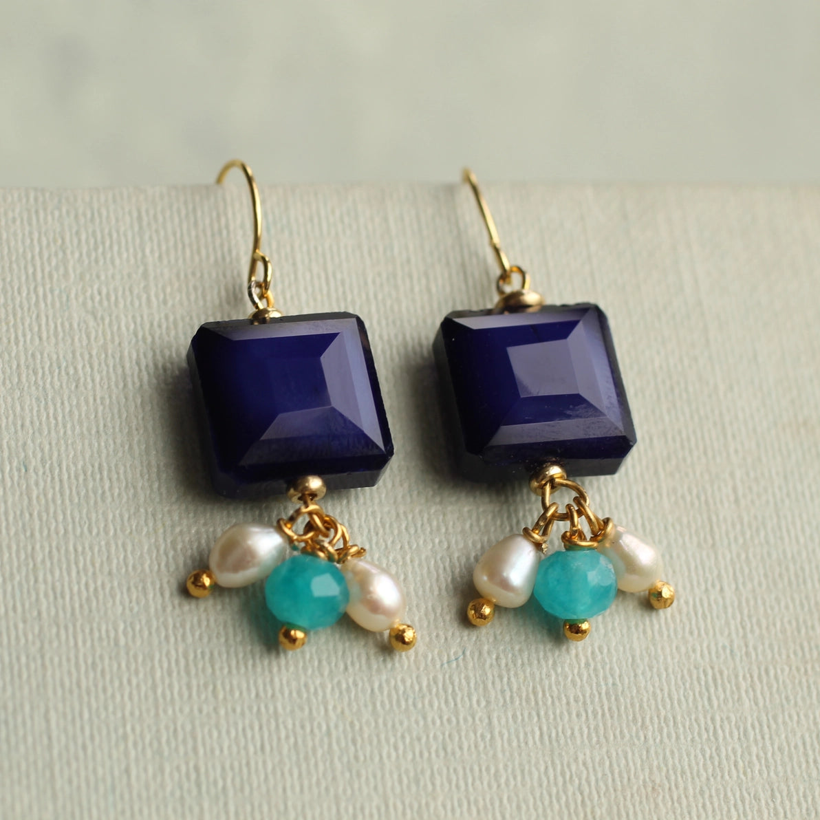 Close-up of Lapis Lazuli charm earrings showing detailed navy square glass tops with dangling aqua, turquoise, and ivory freshwater pearl charms.