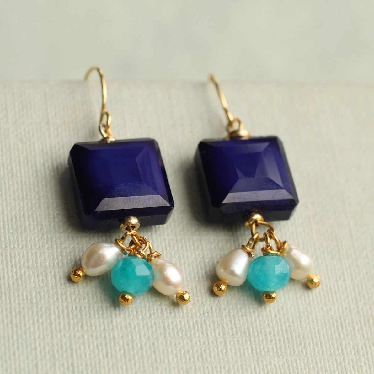 Angled view of Lapis Lazuli blue charm earrings featuring navy glass squares with playful turquoise, aqua opal, and freshwater pearl bead clusters.