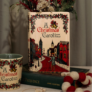 Styled scene with A Christmas Carol vase filled with dried flowers and matching mug.