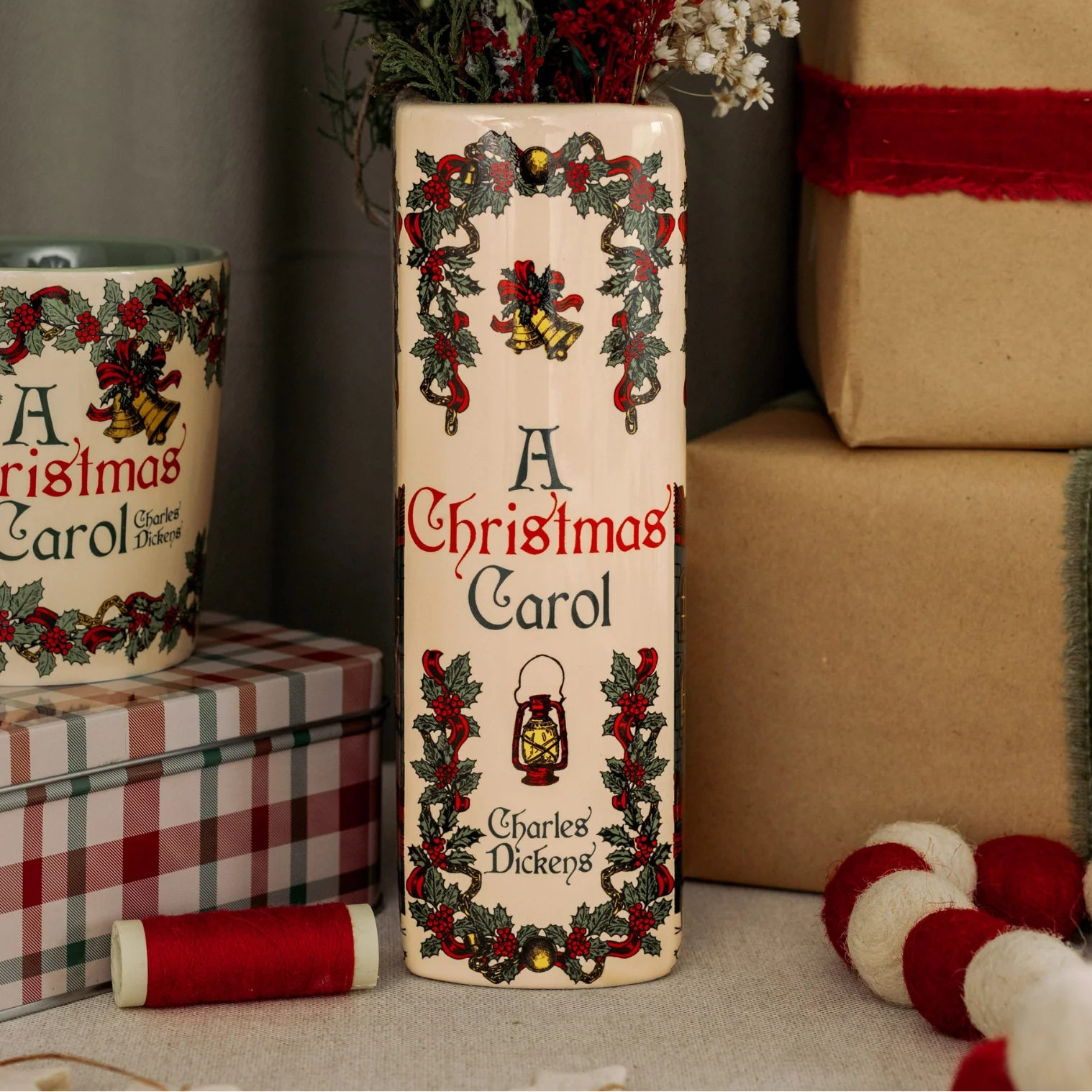 Festive display with A Christmas Carol ceramic book vase, mug, and wrapped gifts.