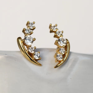 Front-facing view of gold lily of the valley stud earrings resting on a smooth white surface, with sparkling crystal buds arranged along the curved stems.