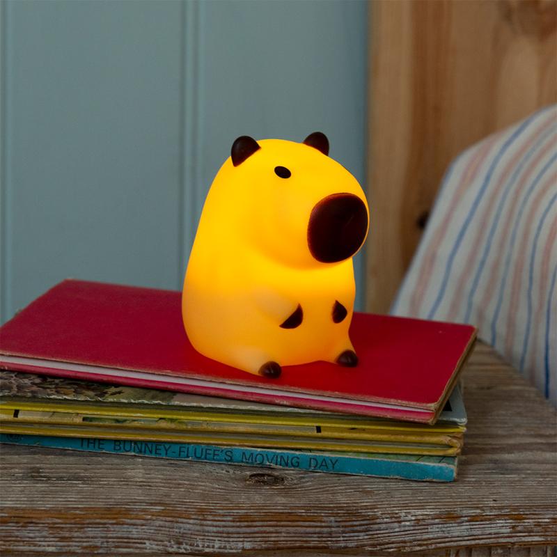 Capybara night light glowing warm yellow on bedside books