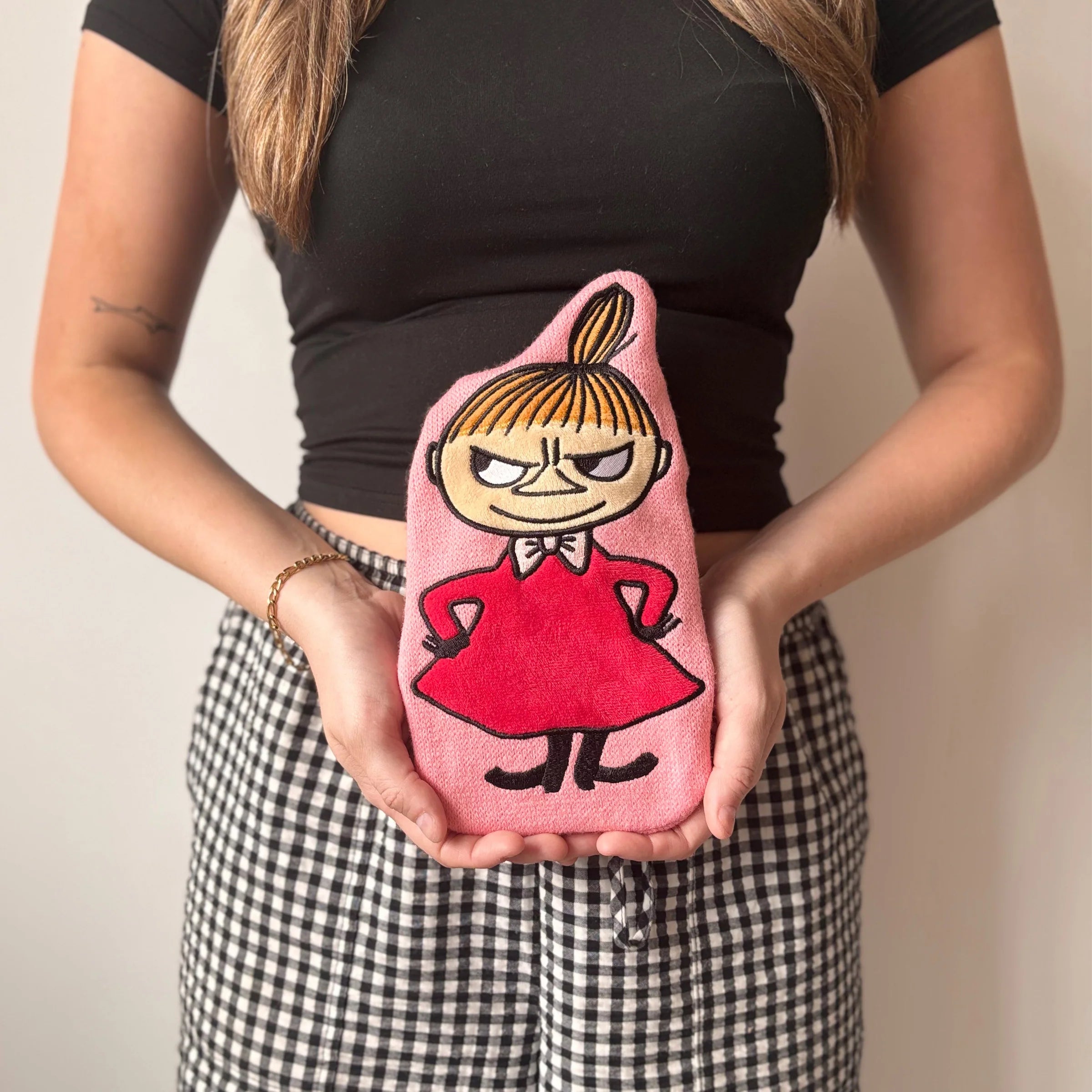 Woman holding Little My Mini Hot Water Bottle against black top.