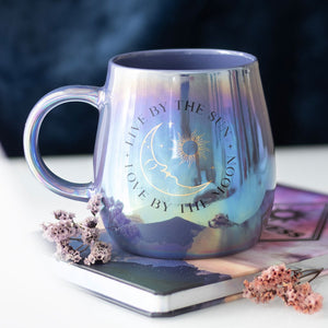 Celestial iridescent mug with moon and sun design on top of a notebook with dried flowers.