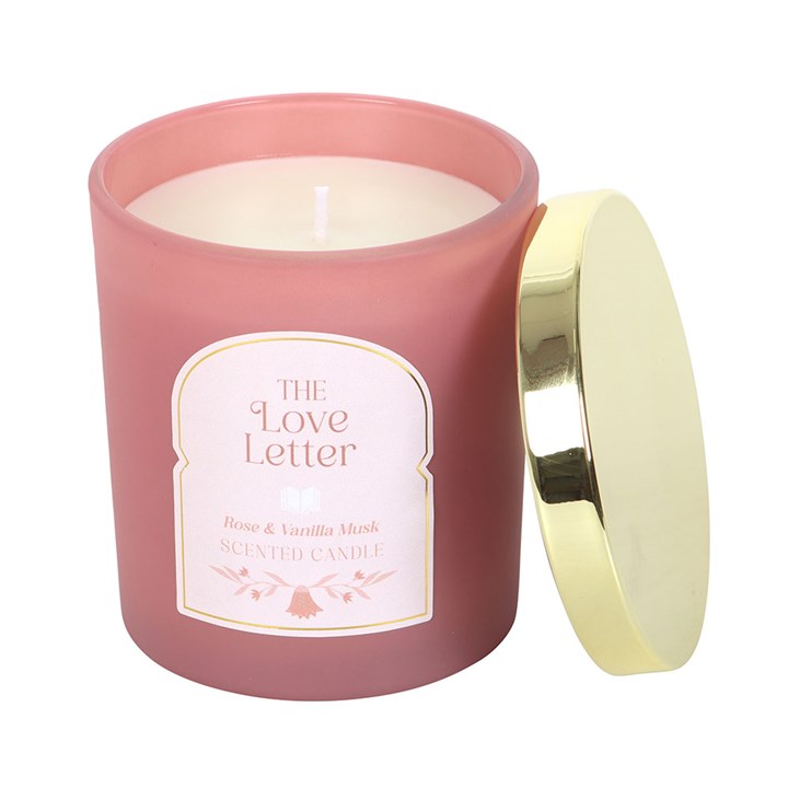 The Love Letter Rose & Vanilla Musk Candle in open pink jar with gold lid resting on the side, showing creamy white wax inside.