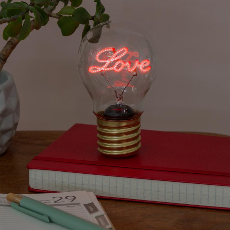 Love light bulb lamp glowing red on desk with book and plant