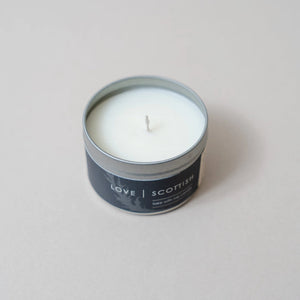 Close-up of Lemongrass candle in a black label tin with “LOVE | SCOTTISH” branding on a minimalist pale background.