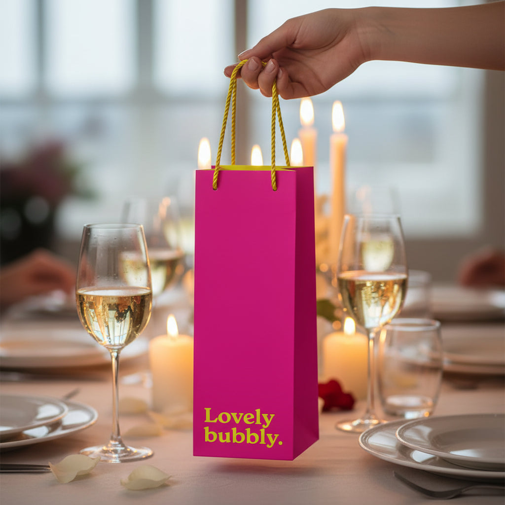 Pink bottle gift bag held by hand over dinner table with champagne glasses
