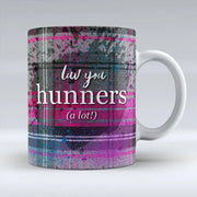 Ceramic mug with bold pink and grey tartan design and the Scottish phrase “Luv You Hunners (a lot!)” in white lettering across the front.