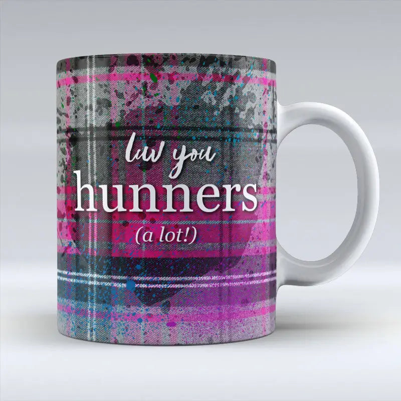 Ceramic mug with bold pink and grey tartan design and the Scottish phrase “Luv You Hunners (a lot!)” in white lettering across the front.