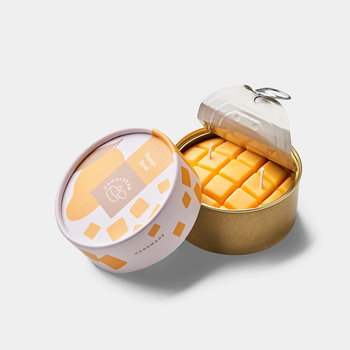 Open mango-scented tin candle with cubed yellow wax and two wicks, designed to look like a real diced mango in a golden food-style can with peel-back lid and colourful packaging.