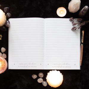 Open manifestation journal showing lined pages with affirmation “I write with intention to manifest my dreams”.