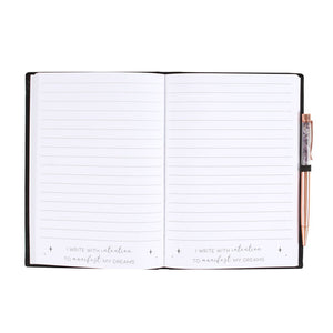Open manifestation journal notebook with lined pages and amethyst crystal pen on side.