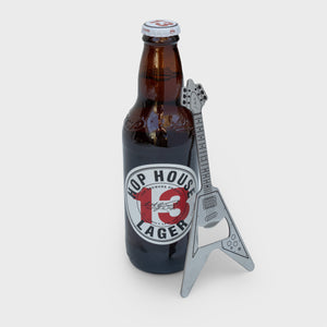 Stainless steel metal guitar bottle opener leaning against a Hop House 13 Lager bottle on a white background.