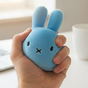 Blue Miffy stress ball squeezed in hand at desk with cup in background