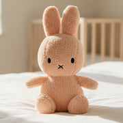Miffy terry peach plush toy sitting on white bedding with wooden cot behind