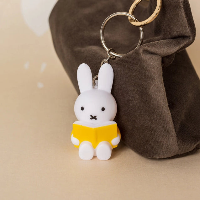 Miffy keyring holding yellow book beside brown velvet pouch on beige background