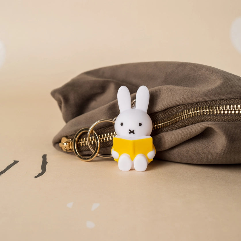 Miffy with book keyring next to brown zippered pouch on beige surface