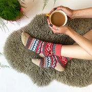 Cosy Fair Isle Moomin socks worn by person holding a mug of tea on a fluffy rug, showing red and pink knit with Little My embroidery.