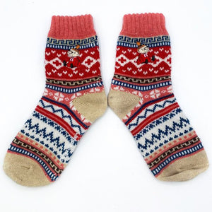 Flat lay of a pair of Fair Isle Moomin socks with Little My embroidery, in red, pink, and biscuit tones with navy and cream accents.