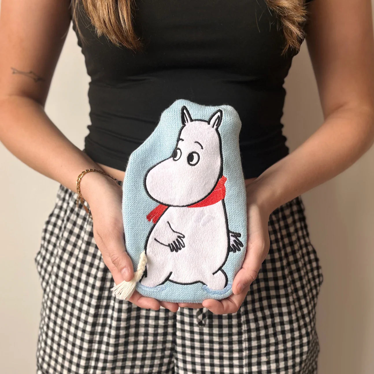 Woman holding Moomin mini hot water bottle in baby blue knit cover with applique patch.