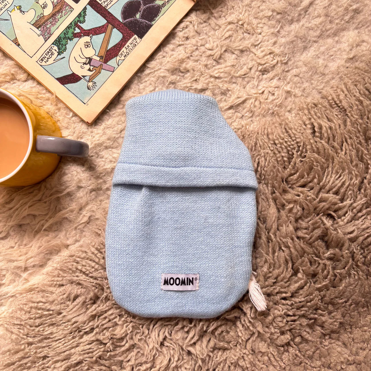 Back view of Moomin mini hot water bottle with baby blue knit cover and Moomin label.