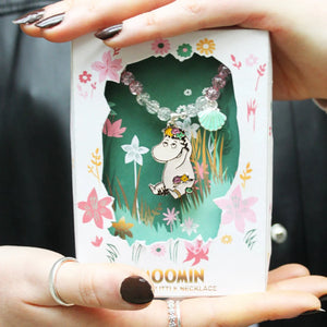 A close-up of a person holding the Moomin Snorkmaiden Enamel Necklace in its decorative box, featuring floral details and a cut-out window displaying the necklace.