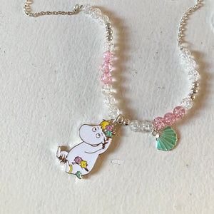 Image 2: The Moomin Snorkmaiden Enamel Necklace laid flat, showcasing its pink and clear beaded chain, green shell charm, and Snorkmaiden pendant.