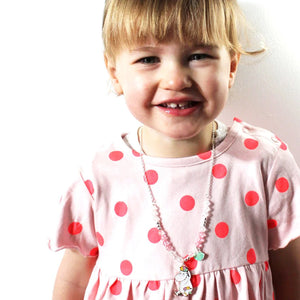 Image 4: A young girl wearing the Moomin Snorkmaiden Enamel Necklace, smiling while dressed in a pink polka dot dress.