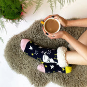 Cosy feet in Moomin star slipper socks with fleece lining, holding a mug on a fluffy rug