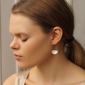 Side profile of a woman wearing gold-plated Mother of Pearl scallop earrings, showing the earrings hanging just below the earlobe with a soft pearlescent glow.