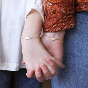 Mother and child holding hands while wearing matching gold flower bracelets.