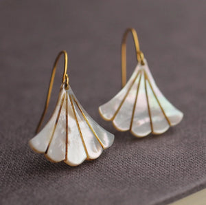 A pair of gold-plated Art Deco earrings featuring carved Mother of Pearl in a scalloped fan shape, displayed against a dark fabric background.