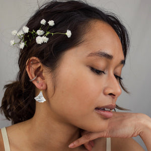 A woman wearing the Mother of Pearl Art Deco earrings with gold-plated ear wires, styled with delicate floral accessories in her hair.