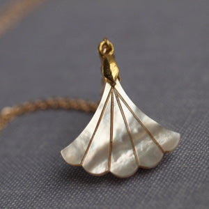 Mother of Pearl fan pendant with a gold-plated chain on a textured fabric background.