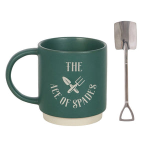 Green ceramic mug with gardening slogan next to silver metal spoon shaped like a garden spade – quirky tea or coffee gift set.