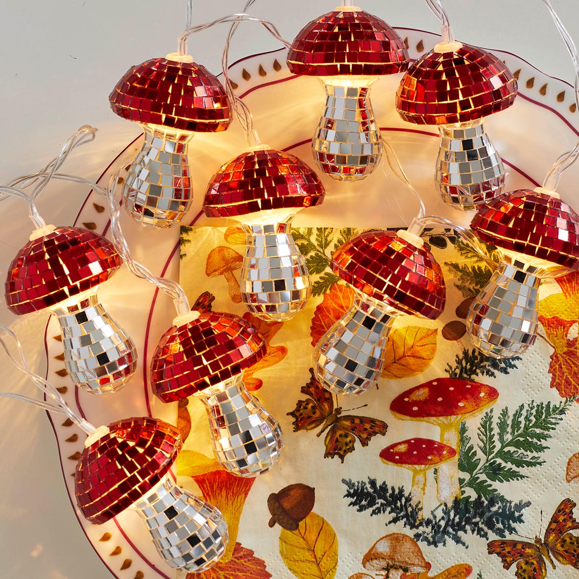 Close-up of Mushroom LED Disco String Lights glowing warmly on a decorative autumn plate.